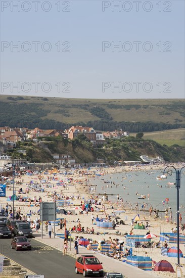 ENGLAND, Dorset, Swanage Bay, Elevated view over busy colourful sandy beach with sunbathers on the sand and swimming in the sea overlooked by hotels.