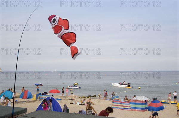 ENGLAND, Dorset, Swanage Bay, Busy colourful sandy beach with sunbathers on the sand and speedboats on the sea. Fish kite blowing in the wind in the foreground.