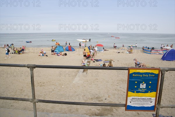 ENGLAND, Dorset, Swanage Bay, View through a railing with a Beach Safety sign towards busy sandy beach with sunbathers on the sand