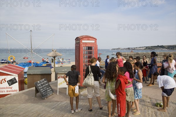 ENGLAND, Dorset, Swanage Bay, A group of children gathered near a traditional red phone box overlooking the beach