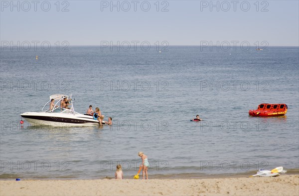 ENGLAND, Dorset, Swanage Bay, Children playing at the waters edge of a sandy beach with people on a speedboat on the sea