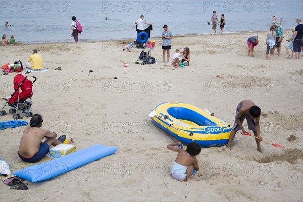 ENGLAND, Dorset, Swanage Bay, Sunbathers and children playing on sandy beach near inflatables and a dingy boat
