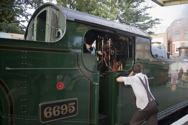 ENGLAND, Dorset, Swanage , Steam Railway. Train driver leaning against train engine waiting in station