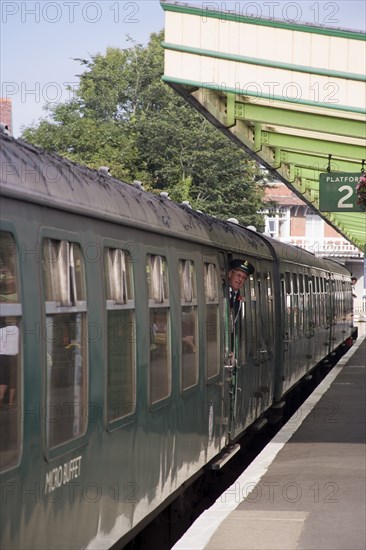 ENGLAND, Dorset, Swanage, Steam Railway Station. View along platform with train departing from station and conductor seen looking out from carriages