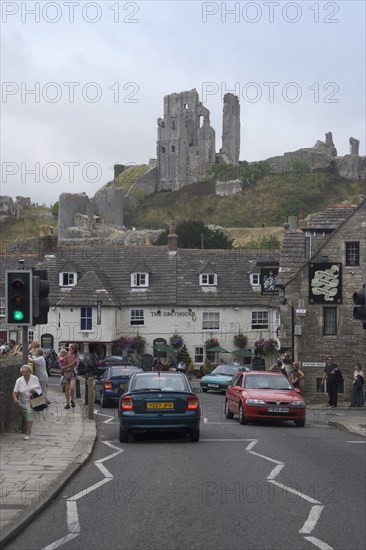 ENGLAND, Dorset, Corfe, View from road with traffic towards cottages overlooked by Corfe Castle behind