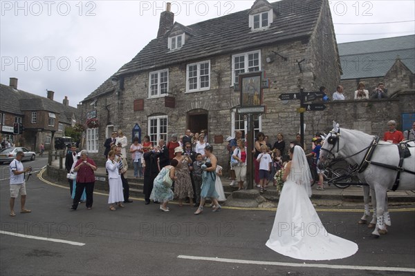 ENGLAND, Dorset, Corfe, A wedding party gathered on the street taking photographs of the bride near a shire horse