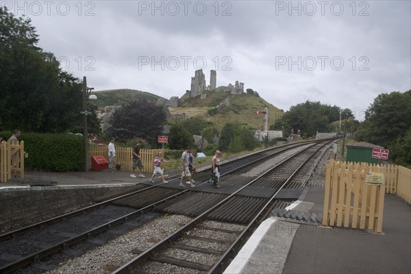 ENGLAND, Dorset, Corfe, People walking over the train line crossing with Corfe Castle behind