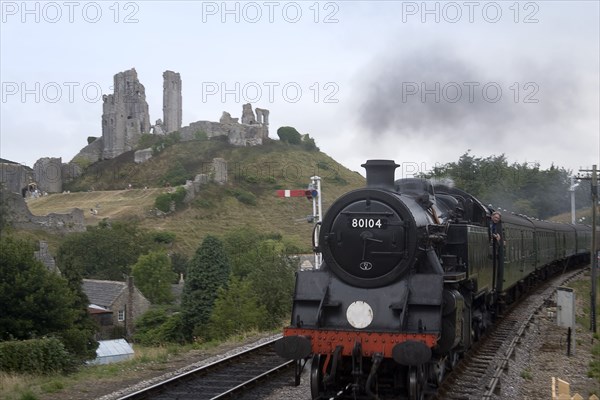 ENGLAND, Dorset, Corfe, Corfe Castle seen behind a railway line with a steam train approaching