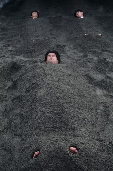 JAPAN, Kyushu, Ibusuki, Sunabulo. Hot Sand Bath with men submerged in sand with only heads and feet showing above surface