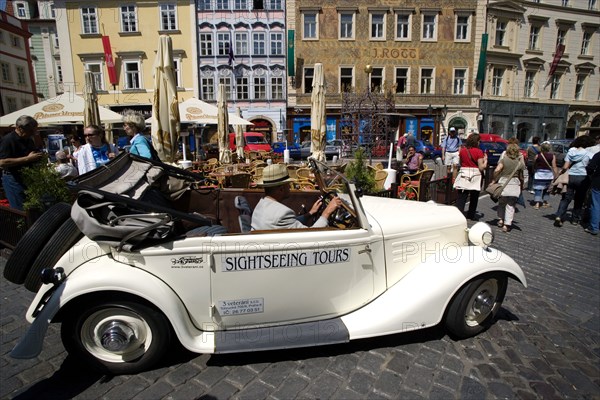 CZECH REPUBLIC, Bohemia, Prague, "Old Town. Vintage open topped car used for sightseeing tours being driven amongst tourists and past a street cafe in Male Namesti, Male Square"