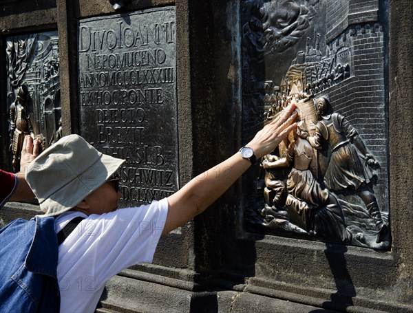 CZECH REPUBLIC, Bohemia, Prague, Tourist touching for luck the relief of the martyrdom of St John Nepomuk on the Charles Bridge