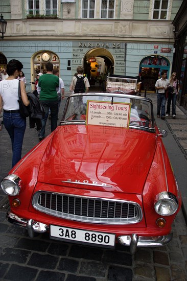 CZECH REPUBLIC, Bohemia, Prague, "Tourists walking past a red Skoda, parked in the street, used for sightseeing tours of the Old Town"