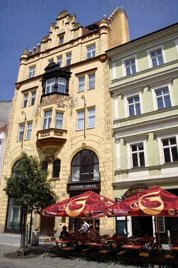 CZECH REPUBLIC, Bohemia, Prague, "Old Town. Tourists sitting at tables under umbrellas outside a cafe with a painted facade in Ovocny trh, the fruit market"