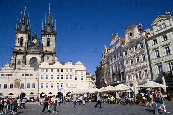 CZECH REPUBLIC, Bohemia, Prague, The Old Town Square with the Church of Our Lady before Tyn. Tourists sit at tables under umbrellas outside cafes and restaurants whilst others stroll in the square.