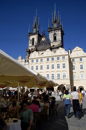 CZECH REPUBLIC, Bohemia, Prague, The Old Town Square with the Church of Our Lady before Tyn. Tourists sit at tables under umbrellas outside cafes and restaurants whilst others stroll in the square