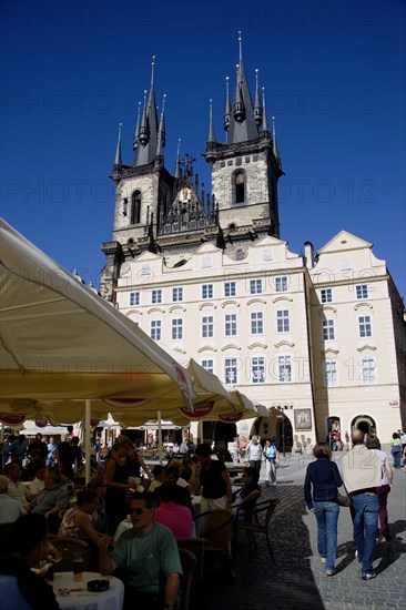 CZECH REPUBLIC, Bohemia, Prague, The Old Town Square with the Church of Our Lady before Tyn. Tourists sit at tables under umbrellas outside cafes and restaurants whilst others stroll in the square