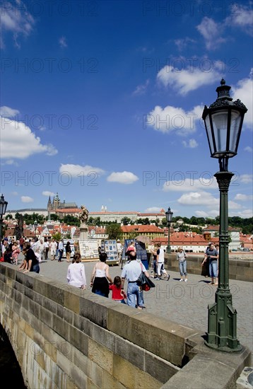 CZECH REPUBLIC, Bohemia, Prague, Tourists on the Charles Bridge across the Vltava River with Prague Castle and St Vitus' Cathedral on the horizon