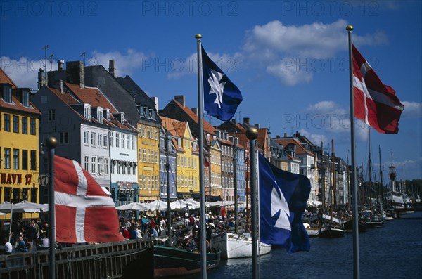 DENMARK , Zealand, Copenhagen, Nyhavn canal with colourful houses along the harbour front. Flags flying in the foreground.