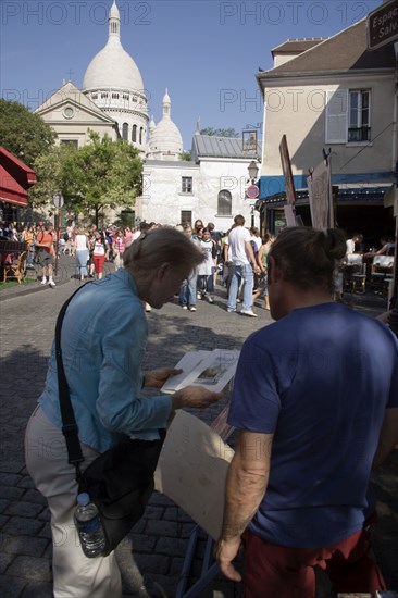 FRANCE, Ile de France, Paris, Montmartre Place du Tertre a square beside the church of Sacre Couer with a tourist discussing a painting with an artist vendor