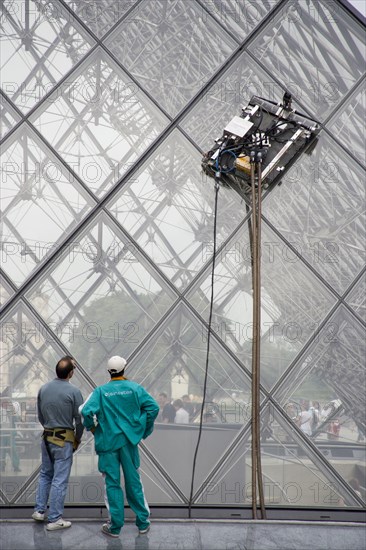 FRANCE, Ile de France, Paris, Workmen watching robot window cleaning machine on the pyramid at the Louvre Museum