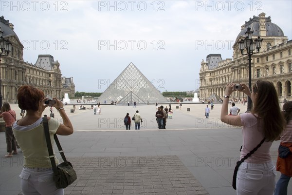 FRANCE, Ile de France, Paris, Tourists taking digital photographs of the pyramid entrance of the Louvre Museum