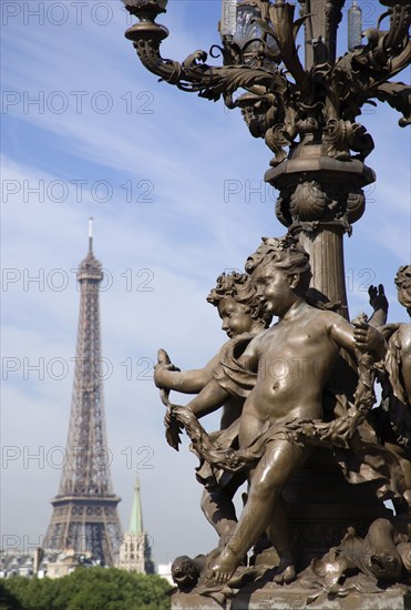 FRANCE, Ile de France, Paris, Ornate bronze lamp-post with cherubs on the Pont Alexandre III bridge across the River Seine with the Eiffel Tower in the distance