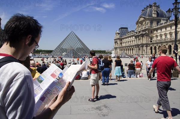FRANCE, Ile de France, Paris, Tourists reading a guide in the square outside the pyramid entrance to the Musee du Louvre