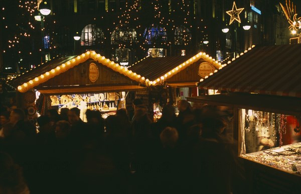 GERMANY, Berlin, Breitscheidplatz. Christmas Market. People gathered around Illuminated stalls at night. Lights and star decorations behind