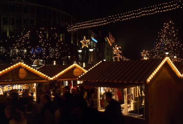 GERMANY, Berlin, Breitscheidplatz. Christmas Market. People gathered around Illuminated stalls at night with lights and star decorations above