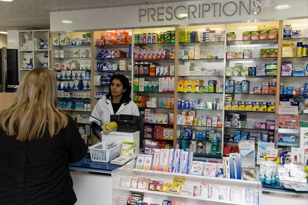 ENGLAND, East Sussex, Shoreham by sea, Interior of high street dispensing chemist  with female customer collecting her prescription from the pharmacist behind the counter