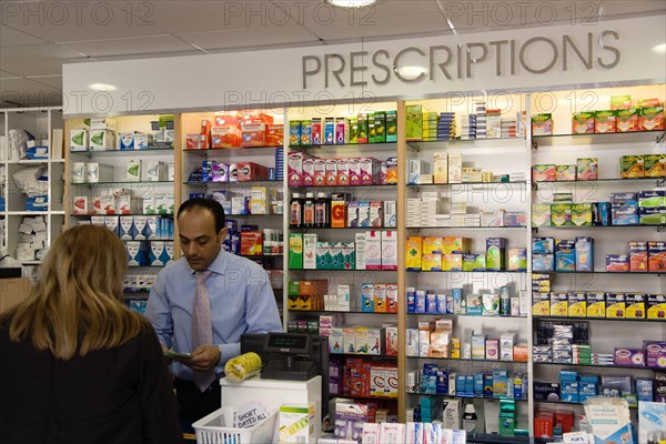ENGLAND, East Sussex, Shoreham by sea, Interior of high street dispensing chemist  with female customer collecting her prescription from the pharmacist assistant behind the counter