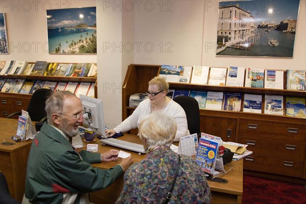 ENGLAND, West Sussex, Chichester, Male and female customer in a Travel Agents office discussing their holiday arrangements with a female travel consultant