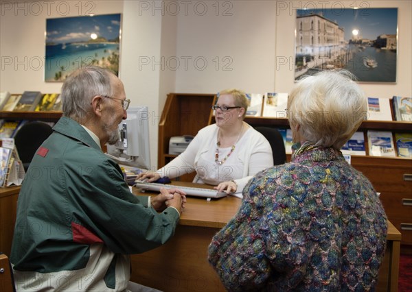 ENGLAND, West Sussex, Chichester, Male and female customer in a Travel Agents office discussing their holiday arrangements with a female travel consultant