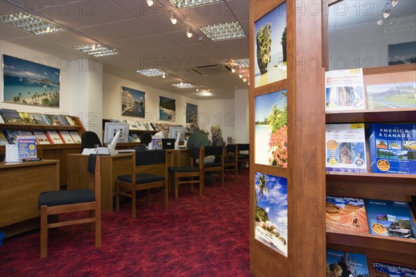 ENGLAND, West Sussex, Chichester, Male and female customer in a Travel Agents office discussing their holiday arrangements with a female travel consultant with travel brochures on shelves in the foreground