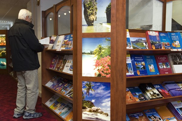 ENGLAND, West Sussex, Chichester, Male customer in a Travel Agents office looking through travel brochures displayed on shelves