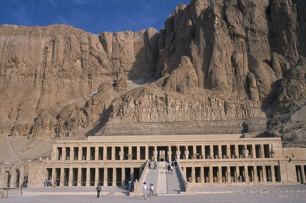 EGYPT, Nile Valley, Thebes, Deir el-Bahri. Hatshepsut Mortuary Temple. Visitors walking towards ramped entrance with limestone cliffs behind.