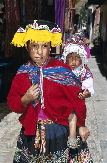 PERU, Near Cusco, Pisac, "Young girl with her sister on her back, Pisac Market."