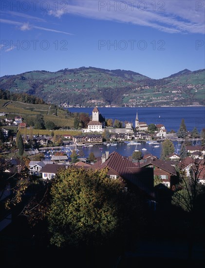 SWITZERLAND, Bernese Oberland, Spiez , View across trees and roof tops towards Spiez Village and the south bank of Lake Thunersee with yachts on the water