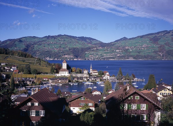 SWITZERLAND, Bernese Oberland, Spiez , View over roof tops towards Spiez Village and south bank of Lake Thunersee with yachts on the water