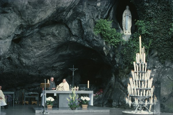 FRANCE, Midi-Pyrenees, Hautes-Pyrenees, Lourdes.  Priest conducting service at cave shrine in pilgrimage centre.