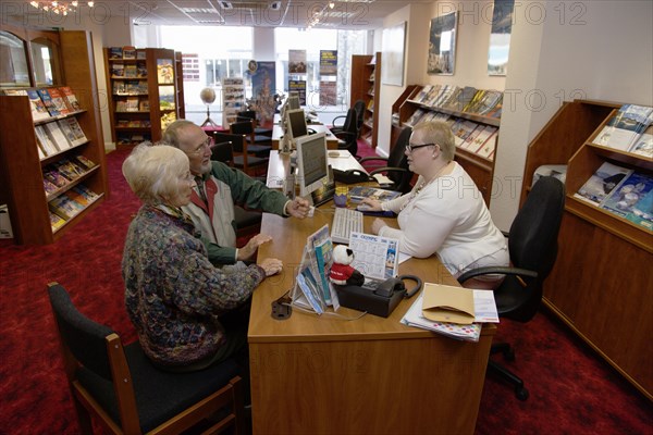 ENGLAND, West Sussex, Chichester, Male and female customer in a Travel Agents office discussing their holiday arrangements with a female travel consultant