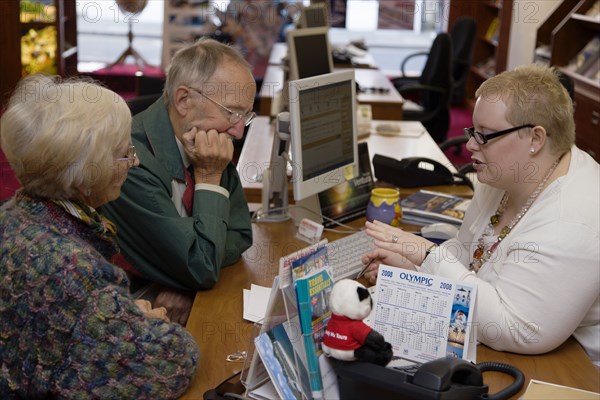 ENGLAND, West Sussex, Chichester, Male and female customer in a Travel Agents office discussing their holiday arrangements with a female travel consultant
