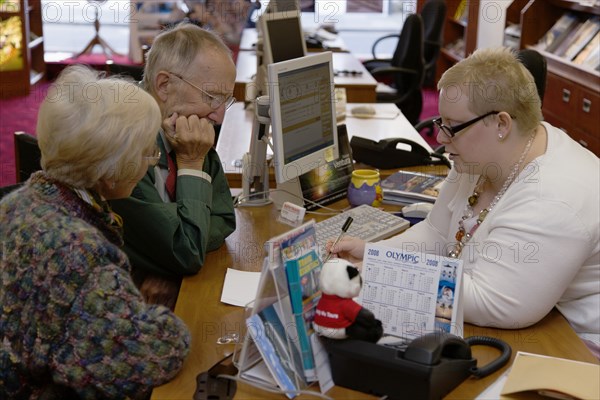 ENGLAND, West Sussex, Chichester, Male and female customer in a Travel Agents office discussing their holiday arrangements with a female travel consultant