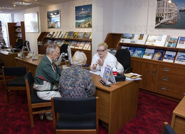 ENGLAND, West Sussex, Chichester, Male and female customer in a Travel Agents office discussing their holiday arrangements with a female travel consultant