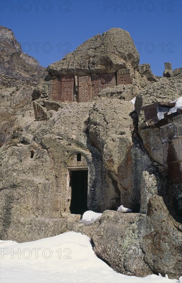 ARMENIA, Geghard, Ancient Geghard Monastery built in the 4th Century AD.  Exterior in snow with carved cross stones set into rock above.