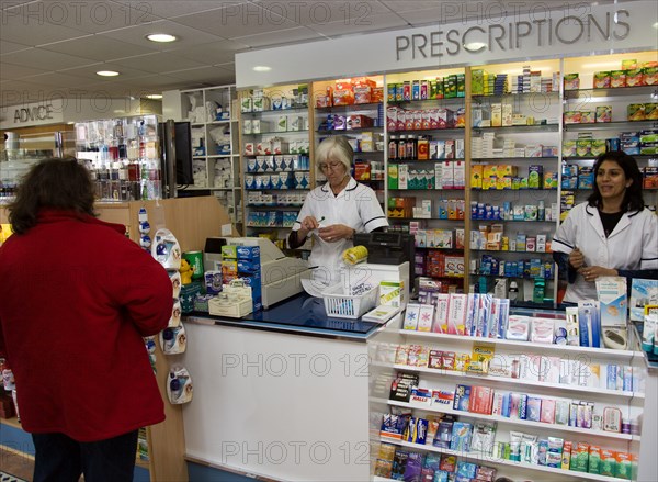 ENGLAND, East Sussex, Shoreham by sea, Interior of high street dispensing chemist  with female customer collecting her prescription from the pharmacist assistant behind the counter