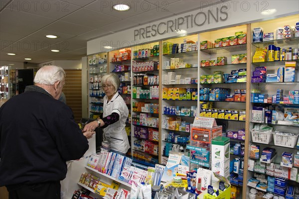 ENGLAND, East Sussex, Shoreham by sea, Interior of high street dispensing chemist  with male customer collecting his prescription from the pharmacist assistant behind the counter