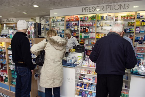ENGLAND, East Sussex, Shoreham by sea, Interior of high street dispensing chemist  with customers collecting prescriptions from the pharmacist assistant behind the counter