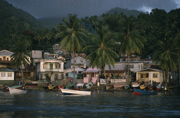 ST LUCIA, Soufriere, "Coastal housing and palm trees with colourful boats pulled up along shore.  Stormy, overcast sky above."