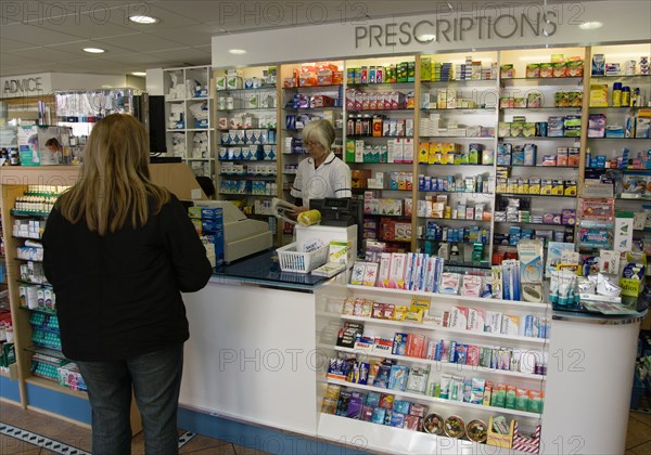 ENGLAND, East Sussex, Shoreham by sea, Interior of high street dispensing chemist  with female customer collecting her prescription from the pharmacist assistant standing behind the counter